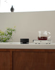 Acaia Horizon sur un plan de travail à côté d’une carafe de café