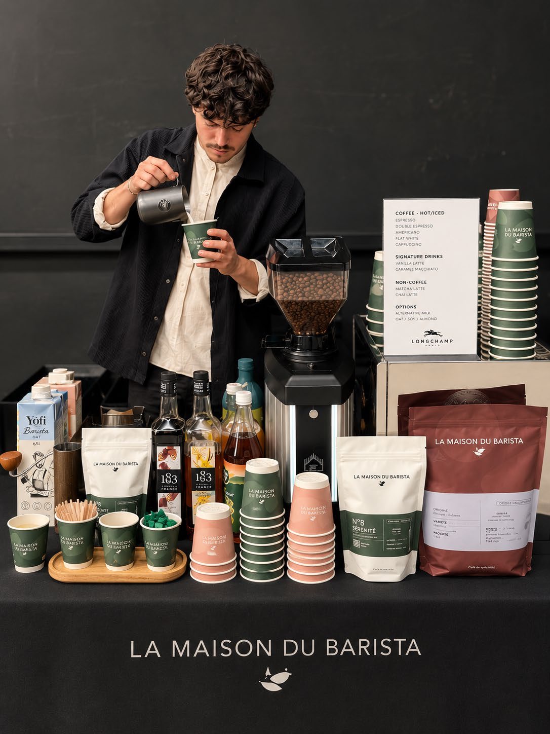 Un barista prépare un latte sur un comptoir événementiel aux couleurs de La Maison du Barista