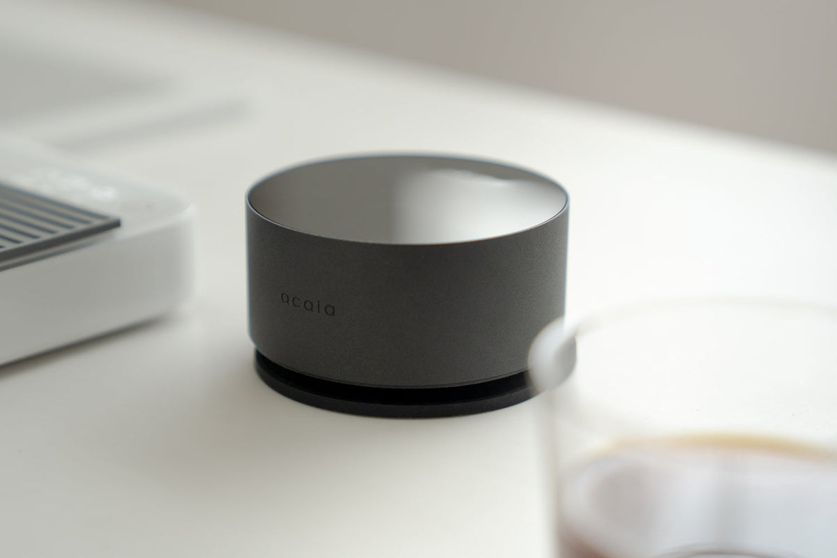 Acaia Horizon posé sur son tapis en silicone à côté d’un verre de café filtre
