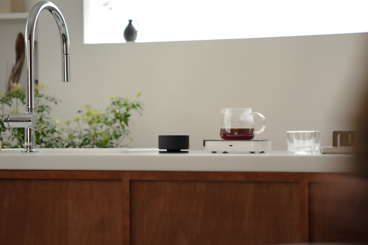 Acaia Horizon sur un plan de travail à côté d’une carafe de café